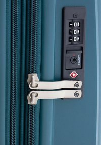 Valigia rigida color teal in primo piano, con zip in metallo, lucchetto TSA a combinazione e doppie zip, che offre sicurezza e durata.
