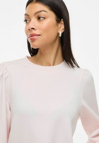 Blusa rosa chiaro con colletto rotondo e maniche a sbuffo. Texture liscia e design minimalista, priva di motivi o elementi hardware visibili.