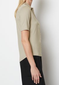 Kortærmet skjorte med knaplukning i lys beige stof. Har klassisk krave, slim fit og buet kant. Glat tekstur.