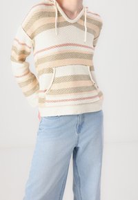 Sweat à capuche avec un tissage texturé, présentant des rayures horizontales beiges, roses et vertes. Inclut une poche frontale et un cordon de serrage.