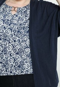 Marinblå kofta över en vit och marinblå topp med swirl-mönster, med en nyckelhålsutskärning och silvrig detalj. Mjuk stickad textur.