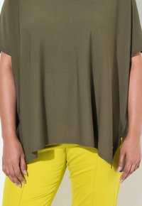 Olivově zelený top s krátkým rukávem a volným střihem, spárovaný s jasně žlutými slim-fit kalhotami. Oba kousky mají hladkou strukturu.