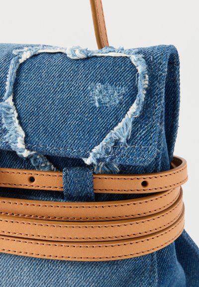 Μπλε τζιν τσάντα με φθαρμένη καρδιά σε σχήμα μπαλώματος στο καπάκι, ασφαλισμένη με διπλό ταμπά δερμάτινο λουράκι με διακοσμητικές ραφές.