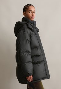 Μαύρο μπουφάν με κουκούλα, με κεντημένες ραφές, ελαστικούς μανσέτες και χαλαρή εφαρμογή. Λείο, γυαλιστερό ύφασμα με ελαφριά εμφάνιση.