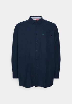 Granatowa koszula z długim rękawem na guziki, z kołnierzykiem i kieszenią na piersi, mała czerwona i biała metka na krawędzi kieszeni.