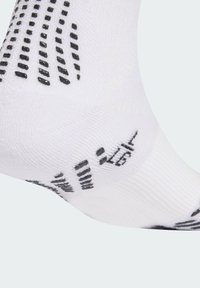 Calcetín deportivo blanco con patrones de agarre negros en la parte inferior, fabricado con un material texturizado y con áreas de refuerzo en el talón y los dedos.