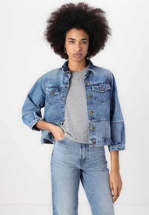 Denim jacket with a faded blue hue, button front, two chest pockets, and rolled sleeves, paired with a grey T-shirt and matching jeans.