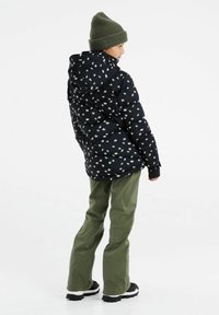 Zwarte pufferjack met wit bloemenpatroon, met capuchon en geribbelde manchetten; gecombineerd met olijfgroene broek en zwarte wandelschoenen.