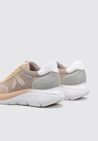 Zapatillas con una parte superior de malla beige y detalles en ante gris, una suela blanca acolchada y detalles de lazo amarillo en los cordones.