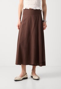 Gonna maxi marrone realizzata in tessuto leggero, con una texture liscia e un design a vita alta, abbinata a flast beige decorate con dettagli.