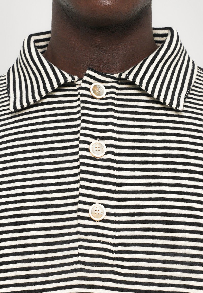 Zwart-witte gestreepte polo met een kraag en een knoopsluiting van drie knopen. De stof heeft een gladde textuur en is gebreid.