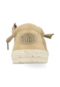Zapato sin cordones de ante beige con un respaldo de tejido texturizado, suela beige moteada y logotipo "HEY DUDE" en el talón. Presenta una puntera redondeada y un diseño ligero.