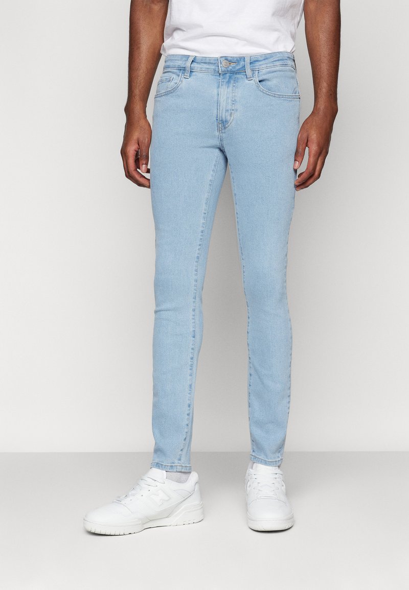 Vaqueros skinny de un azul claro, hechos de denim, con un diseño de cinco bolsillos, costuras sutiles y una cintura de altura media, combinados con zapatillas blancas.