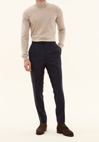 Lys beige rullekrave sweater og mørk marineblå skræddersyede bukser med knaplukning og sidelommer, suppleret med brune ruskinds ankelstøvler.