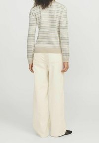 Maglione a righe beige, con sottili linee orizzontali blu e verde, abbinato a pantaloni a gamba larga di colore chiaro e ballerine nere.