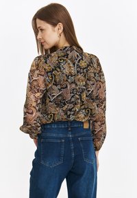Przezroczysta kwiatowa bluzka w czerni z ziemistymi odcieniami; zebrane rękawy i tył. Połączona z dżinsami w kolorze niebieskim o wysokim stanem.