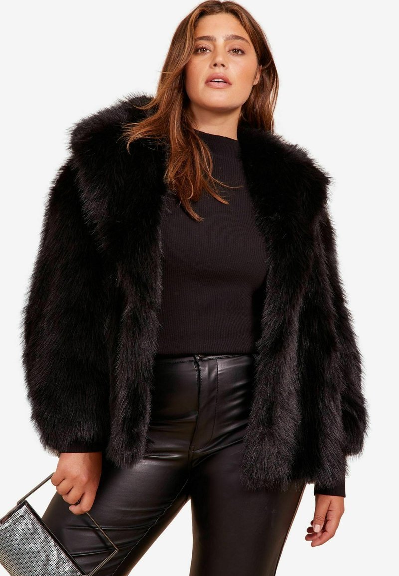 Jachetă din blană artificială neagră cu glugă, având o textură pufoasă și mâneci largi. Combinată cu un top negru cu danteluri și pantaloni din piele.