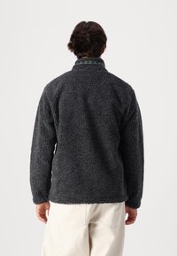 Dark gray fleece jacket with a textured surface, featuring a high collar and a decorative patterned trim at the neck. Casual fit.