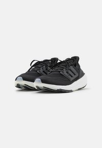 Scarpe sportive nere con tomaia texturizzata, tre strisce laterali e suola intermedia bianca. Presentano lacci neri e una suola in gomma con dettagli antiscivolo.