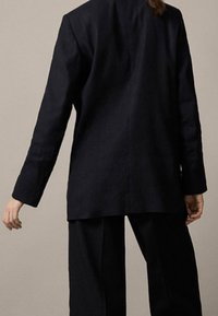 Dunkelblauer Navy-Blazer mit tailliertem Schnitt, langen Ärmeln und geradem Schnitt. Hergestellt aus einem strukturierten Stoff mit minimalen Details.