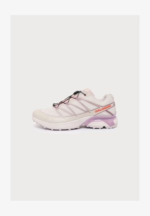 Chaussure de course Salomon rose clair et blanche avec système de laçage rapide noir, détail violet sur la semelle et logo Salomon rouge sur le côté.