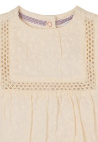 Blouse de couleur crème avec un motif floral, décolleté carré avec des détails en dentelle et tissu froncé en bas.