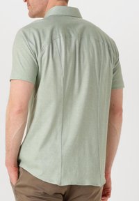 Korte mouwen shirt van lichtgroene stof met een kraag. Heeft subtiele zijnaad en een gebogen zoom. Gladde textuur, casual ontwerp.