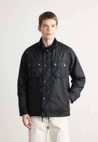 Black jacket with a corduroy collar, snap buttons, two chest pockets, and zippers, featuring a smooth texture and a relaxed fit.