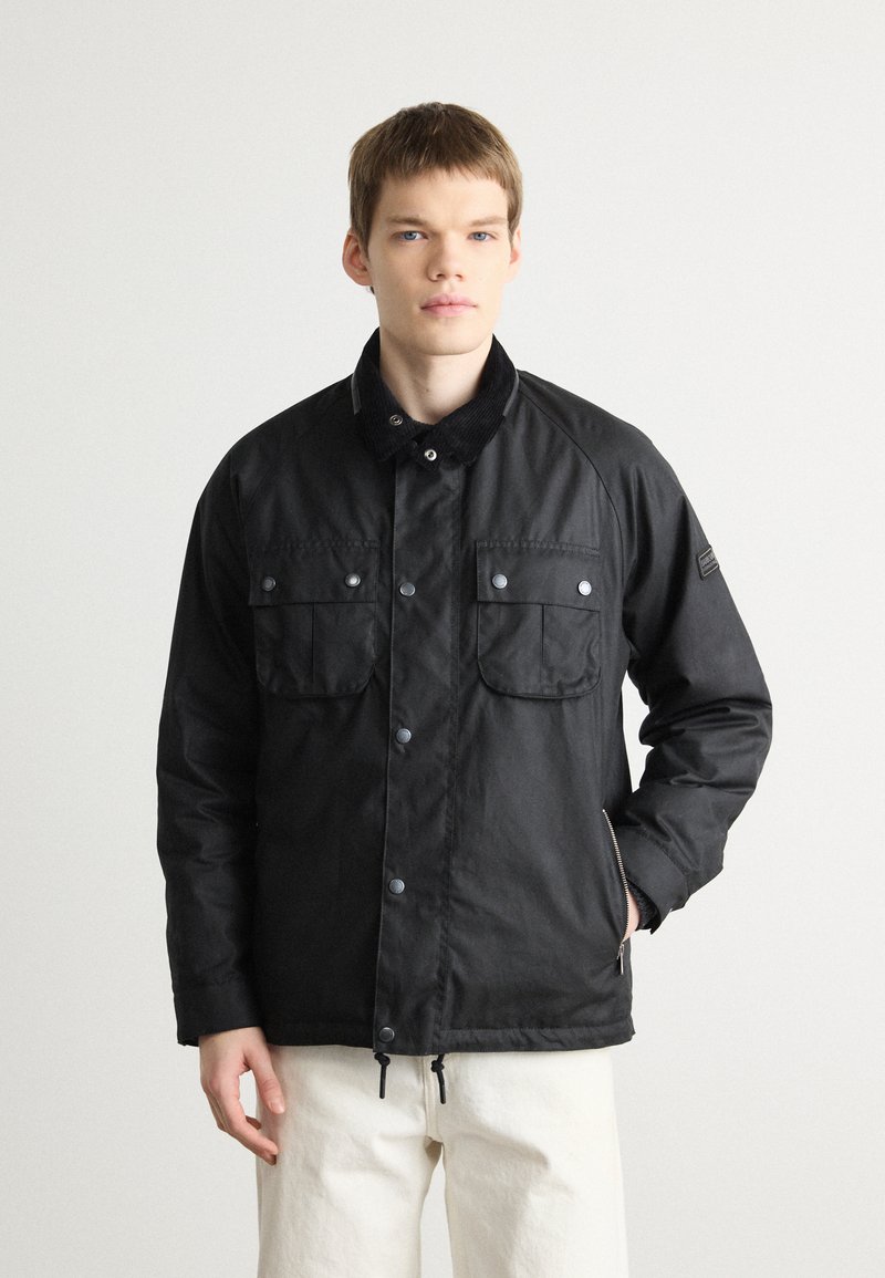 Black jacket with a corduroy collar, snap buttons, two chest pockets, and zippers, featuring a smooth texture and a relaxed fit.