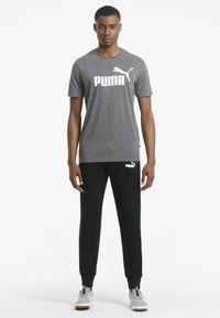 Grå atletisk t-shirt med hvid "PUMA" logo, parret med sorte joggers med hvidt mærke-logo; begge lavet af letvægtsstof.