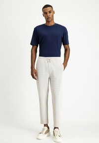 T-shirt blu navy a maniche corte abbinato a pantaloni della tuta grigio chiaro con coulisse, caratterizzati da una texture a costine, e sneaker bianche con dettagli beige.