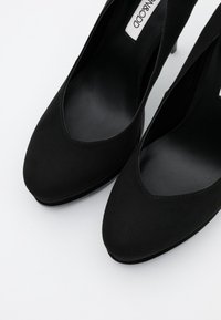 Svarta mocka högklackade skor med spetsig tå och utskärning på sidan, med en slät innervaddering och en smal klack.