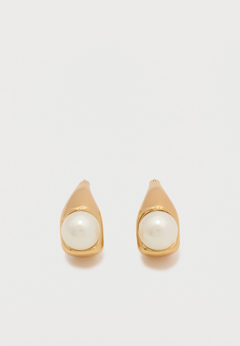 Σκουλαρίκια καρφάκια σε χρυσό τόνο, το καθένα με μία στρογγυλή λευκή πέρλα, τοποθετημένη σε λείο, κυρτό μέταλλο σε απλό φωτεινό φόντο.