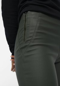 Højtaljede, mørkegrønne faux læderbukser med lynlås i siden og tætsiddende design, der har synlige sømme og en glat tekstur.