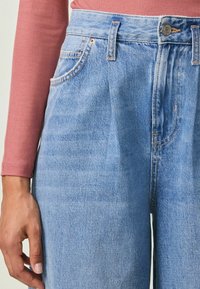 Kõrgendatud vöökoht, helesinised denim püksid, millel on lõdva sobivus, delikaatsed kulunud kohad, vasknõelad ja tikkimisega taskud.