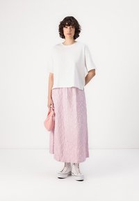 Hvit kortermet t-skjorte, teksturert rosa maxiskjørt, hvite høye sneakers og en liten rosa håndveske. Enkelt, uformelt design.
