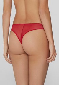 Rote durchsichtige Slips mit einem weichen elastischen Bund und minimaler Bedeckung bei glatter Textur.