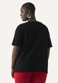Camiseta negra de manga corta con un ajuste relajado, cuello redondo y tejido suave, combinada con pantalones rojos ajustados.