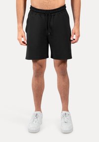 Pantalones cortos negros con cintura elástica y cordón, con una tela suave y un diseño de pierna recta. Combinados con zapatillas blancas.