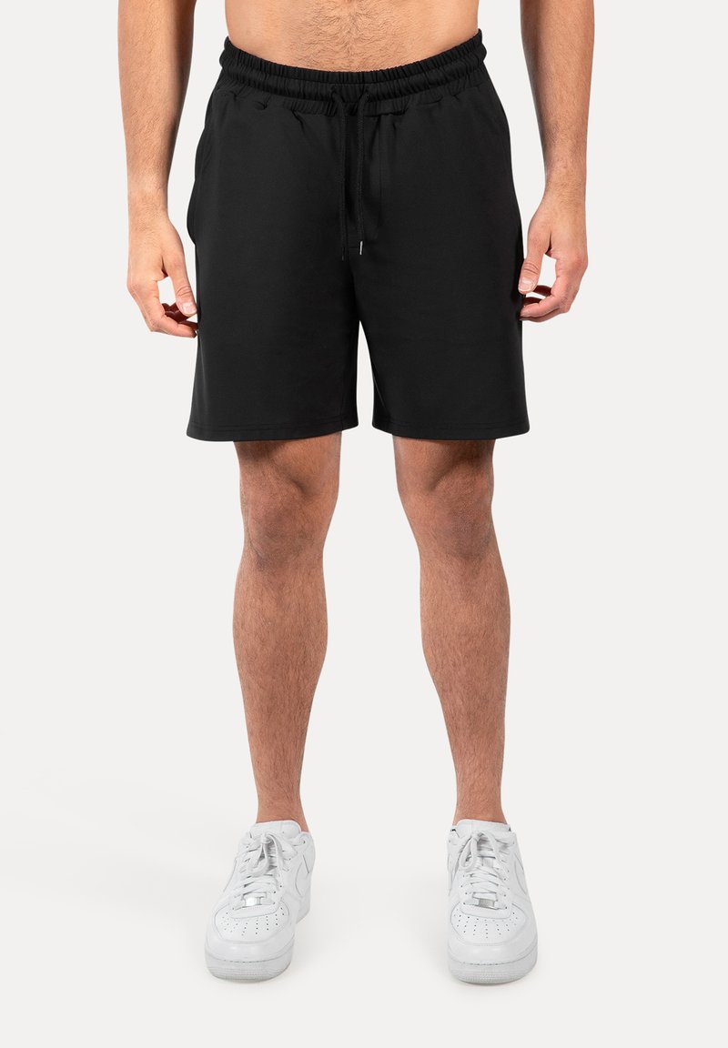 Pantalones cortos negros con cintura elástica y cordón, con una tela suave y un diseño de pierna recta. Combinados con zapatillas blancas.