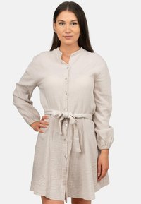 Abito button-up color beige chiaro con colletto strutturato, maniche lunghe e una cintura in tessuto, caratterizzato da un motivo testurizzato e un leggero luccichio.