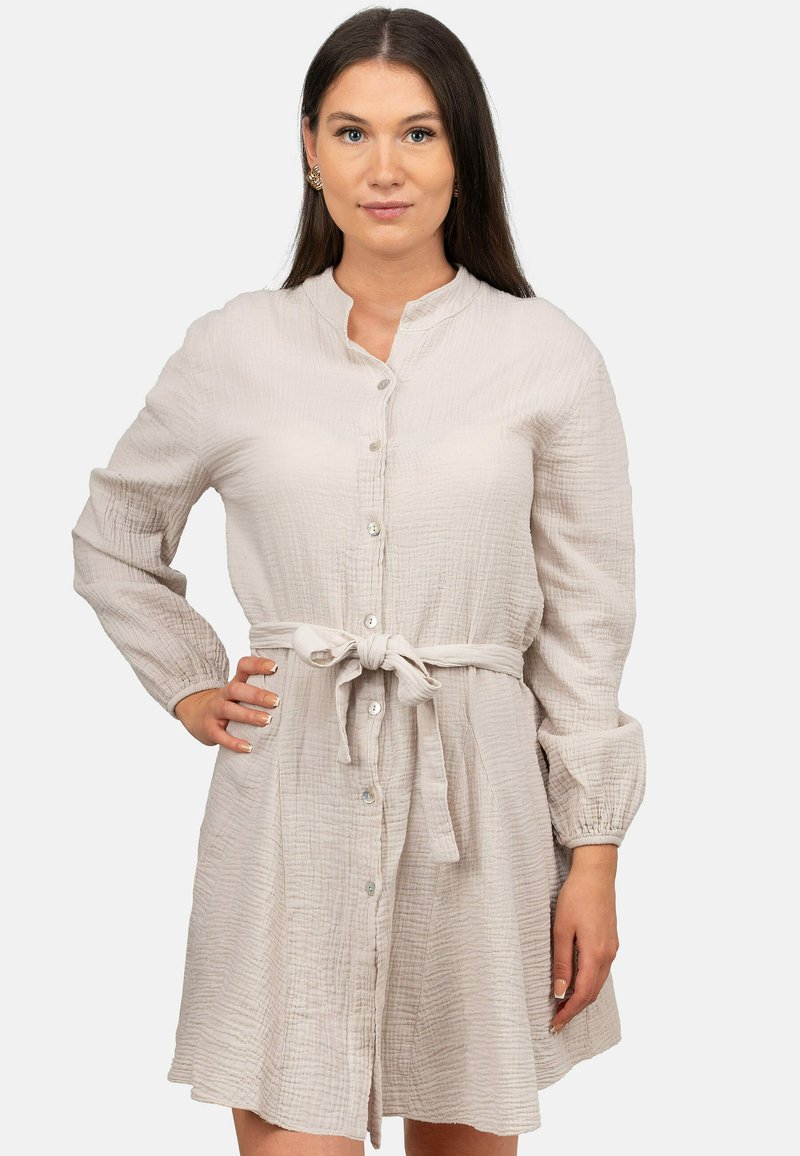 Abito button-up color beige chiaro con colletto strutturato, maniche lunghe e una cintura in tessuto, caratterizzato da un motivo testurizzato e un leggero luccichio.