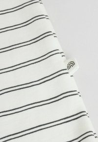 Tissu rayé en blanc et noir avec une texture douce. Comprend une petite étiquette avec un design circulaire sur le bord.