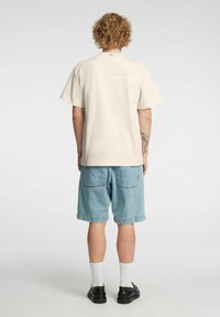 Helebee�žist puuvillane t-särk lühikeste varrukatega, millel on tagaküljel reljeefsed tähed. Kandmiseks sobivad hele sinised teksapüksid ja mustad kingad.