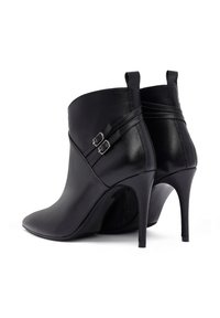 Schwarze Leder-Stiefeletten mit spitzem Zeh, hohen Stilettos und dekorativen Schnallenriemen. Geschmeidige Textur mit schlankem Design.