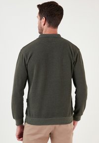 Donkergroene, ribgebreide polo trui met lange mouwen, een kraag en een rechte zoom. Minimalistisch ontwerp, geen zichtbare logo's of patronen.