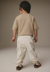Beige kortærmet skjorte, hvide cargo bukser med elastiske manchetter og multicolor sneakers. Synlige syning-detaljer og lommer på bukserne.