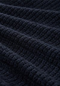 Tissu tricoté bleu marine avec une surface texturée et à motifs, mettant en valeur des ondulations en relief et un aspect doux et tissé.
