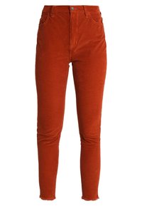 Pantalon en velours côtelé couleur rouille avec taille haute, poches avant, fermeture par bouton, et jambes fines effilées avec ourlets bruts.