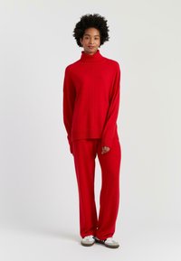 Maglione rosso a maglia con colletto alto, vestibilità rilassata e maniche lunghe abbinato a pantaloni a gamba larga coordinati. Tessuto a trama, design senza cuciture.